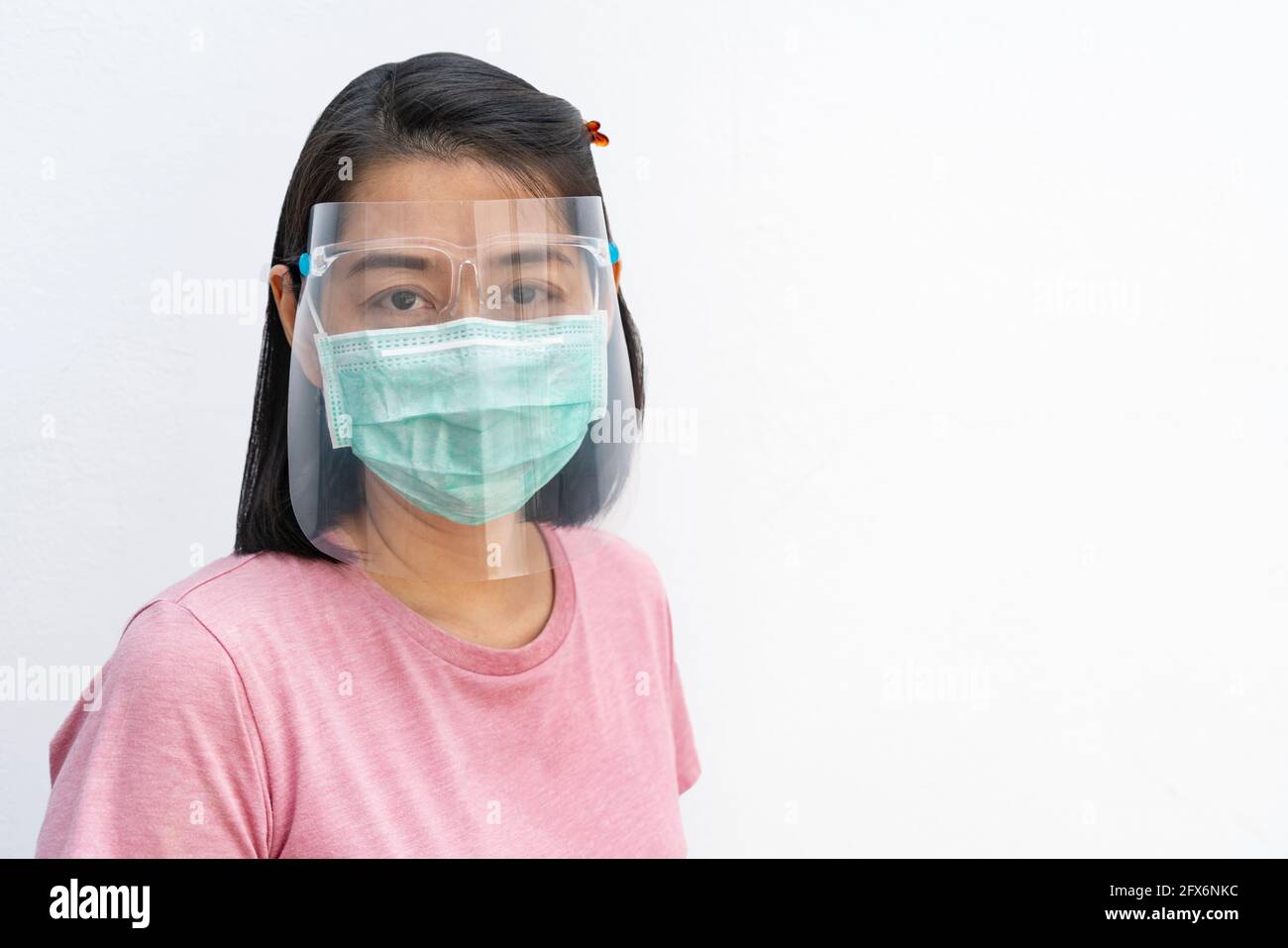 Porträt einer asiatischen Frau mittleren Alters, die medizinische Gesichtsmaske und Gesichtsschutz trägt, schwarzes kurzes Haar und T-Shirt trägt, auf Kamera schaut, isoliertes Bild Stockfoto