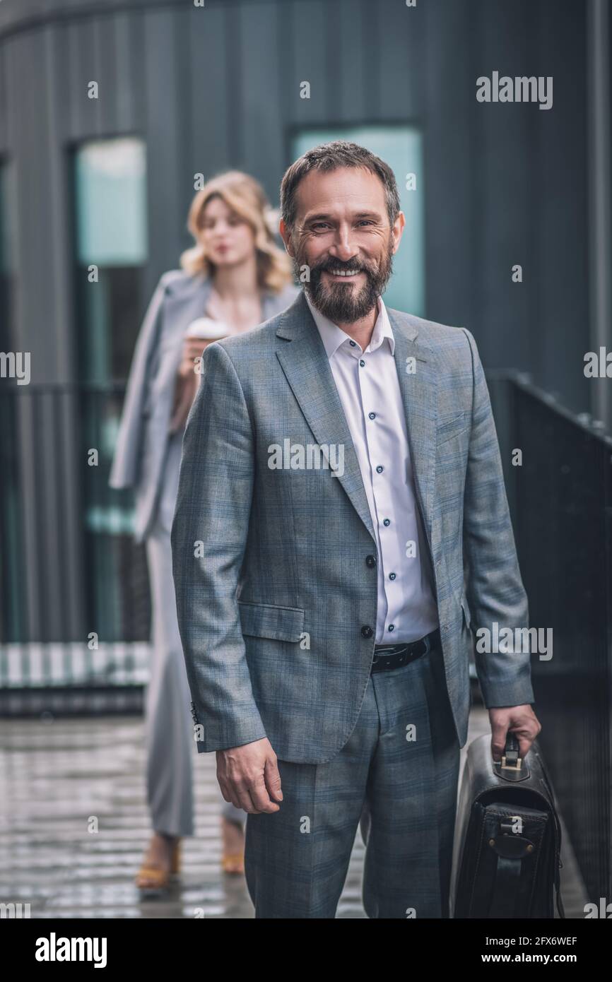 Fröhlicher Mann, der in der Nähe des Büros und einer Frau hinter sich herumläuft Stockfoto