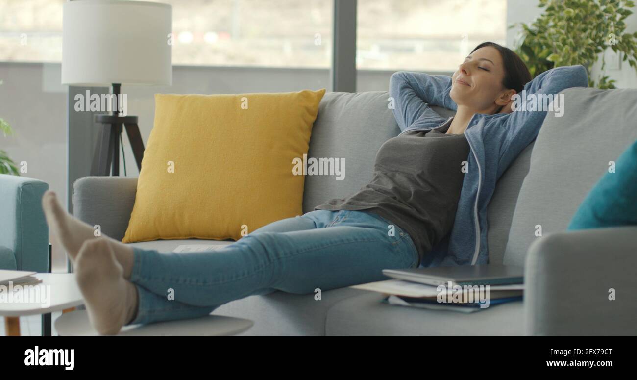 Frau, die eine Pause macht und sich auf der Couch ausruht, schläft mit den Händen hinter dem Kopf Stockfoto