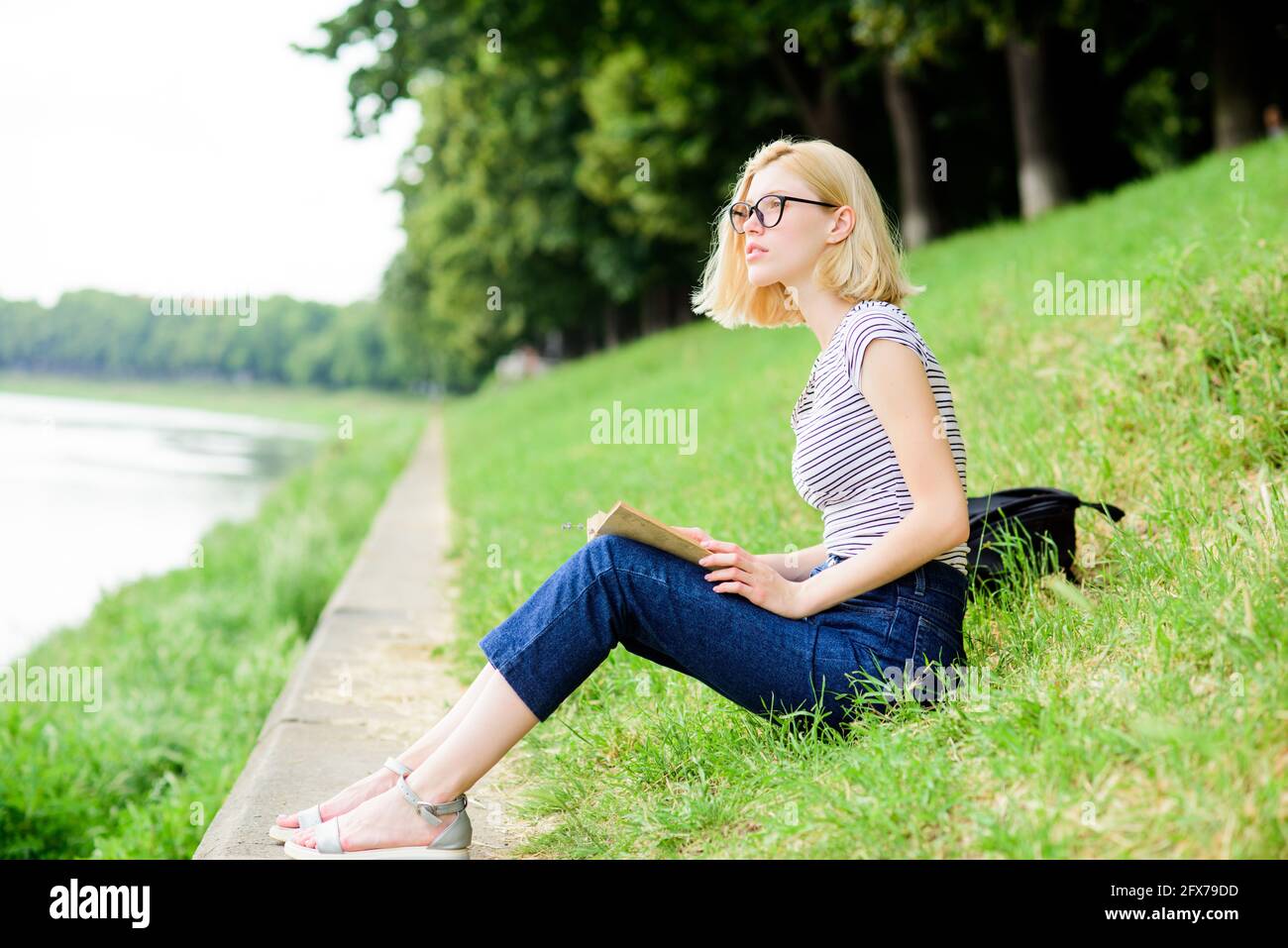 Mädchen, die sich nach einem Arbeitstag am Fluss entspannen. Frau träumt vom Urlaub. Ruhe Entspannung und Hobby. Verbringen Sie Freizeit für sich selbst. Mädchen sitzen auf grün Stockfoto