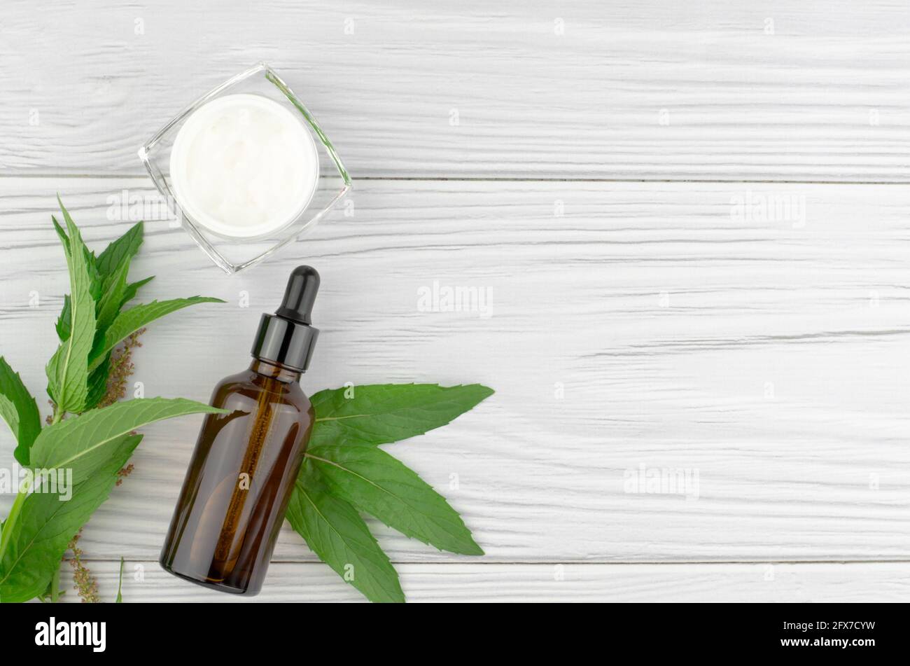 Creme, Kräuter und eine dunkle Glasflasche auf hellem Holzhintergrund. Flach liegend, Draufsicht, Kopierbereich. Konzept der Hautpflege und Schönheitsbehandlung Stockfoto