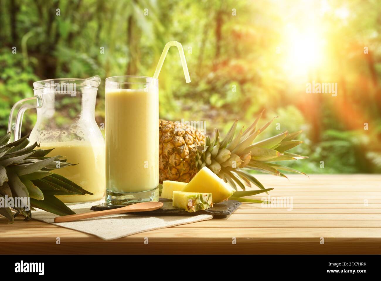 Gläser mit Ananassaft mit Milch- und Ananasportionen auf Holztisch und tropischem Hintergrund. Vorderansicht. Stockfoto