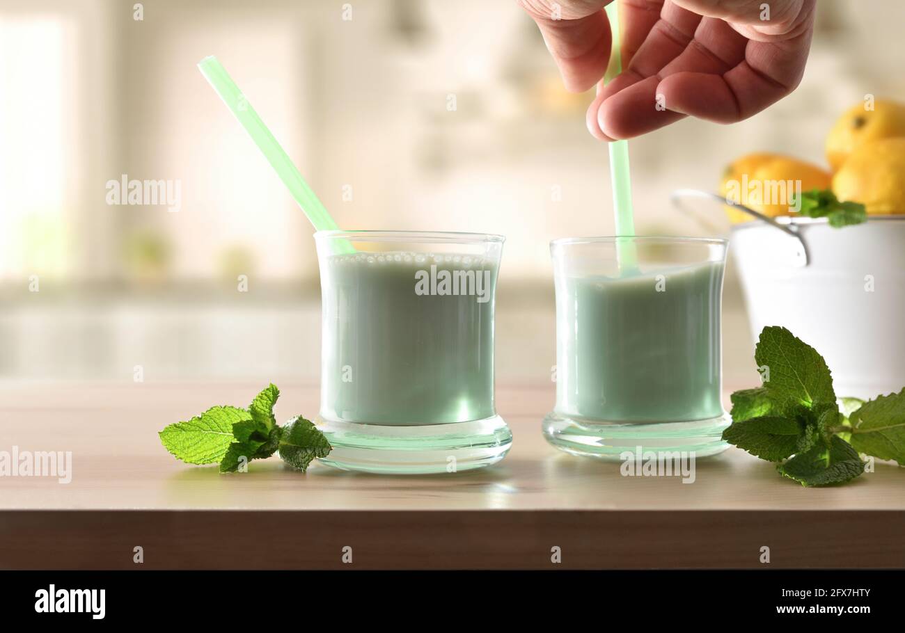 Mann, der Minzmilchgetränk mit Stroh auf einer Küchenbank mischte. Vorderansicht. Stockfoto