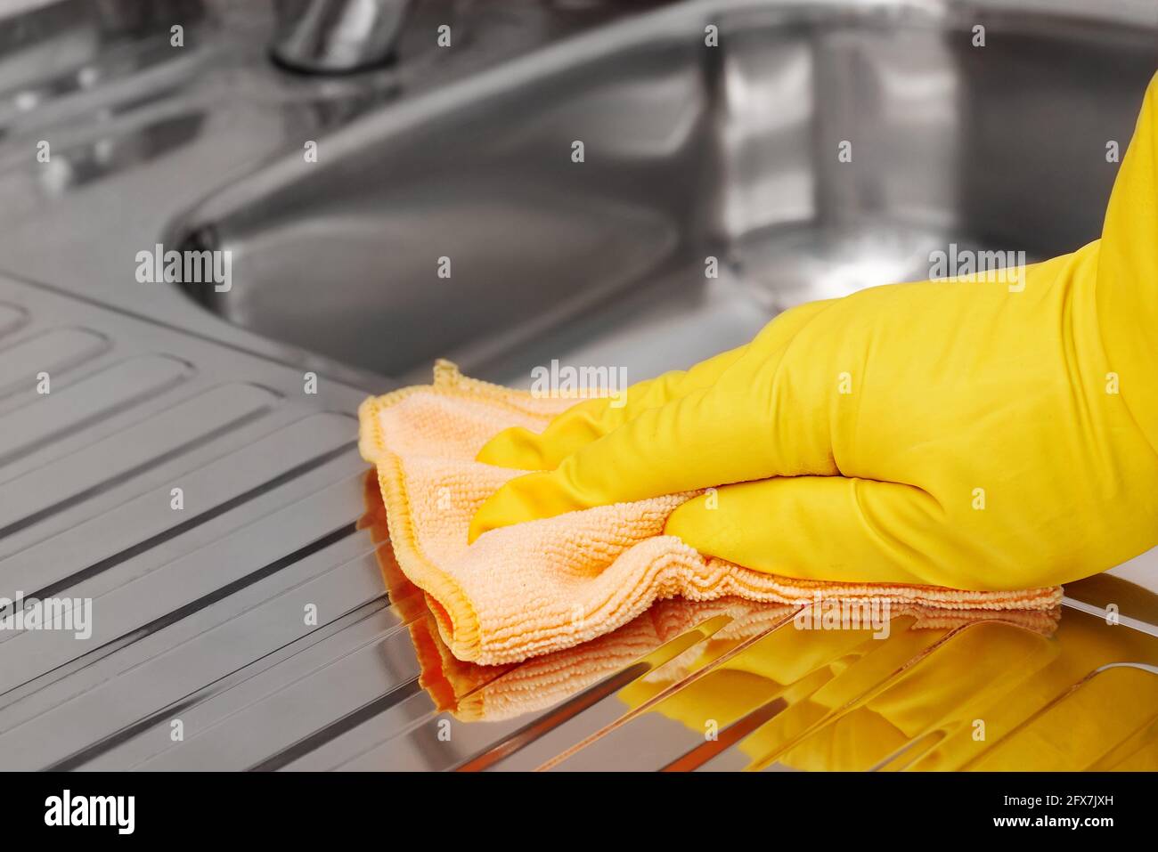 Hand in gelbem Latex Schutzhandschuh zum Abwischen des Edelstahlwaschbeckens mit Mikrofasertuch. Haushaltsreinigungsgeräte. Stockfoto