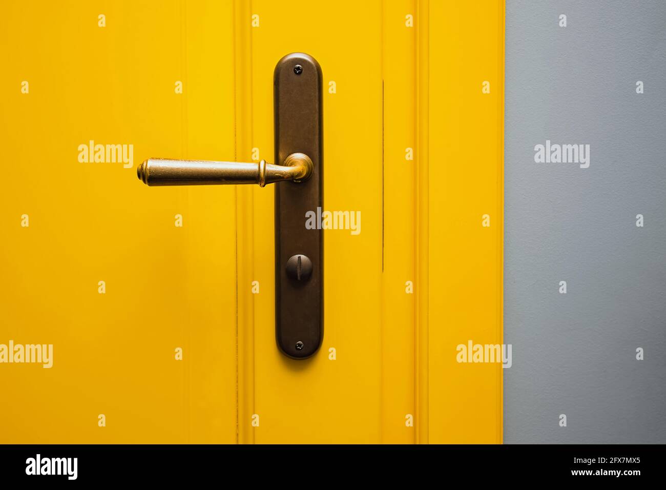 Gelbe Tür mit einem bronzenen Türgriff in Nahaufnahme. Stockfoto