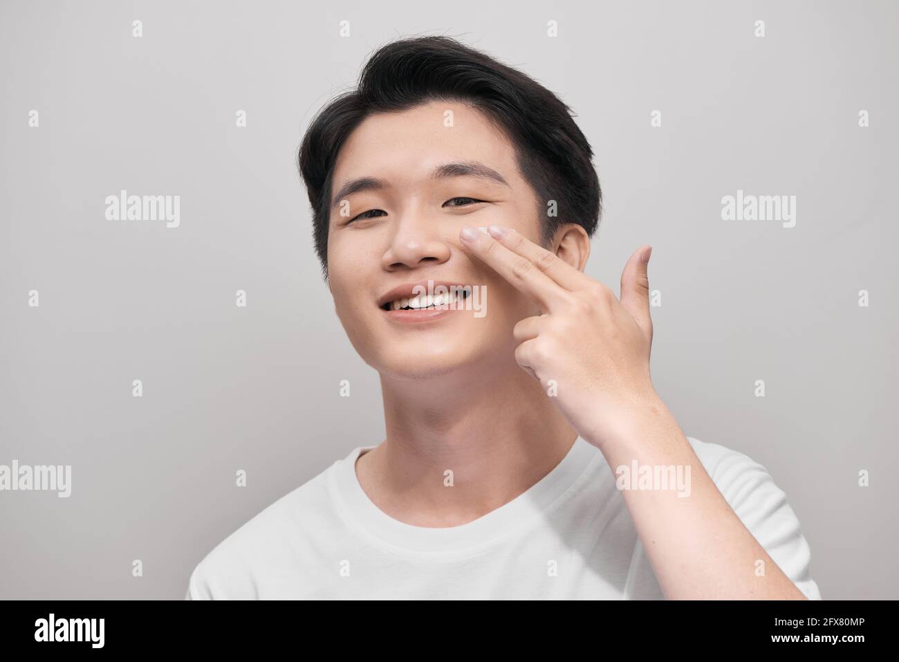 Pflege, Hautpflege und Menschen Konzept - lächelnden jungen indischen Mann Anwendung Creme auf Gesicht über weißem Hintergrund Stockfoto