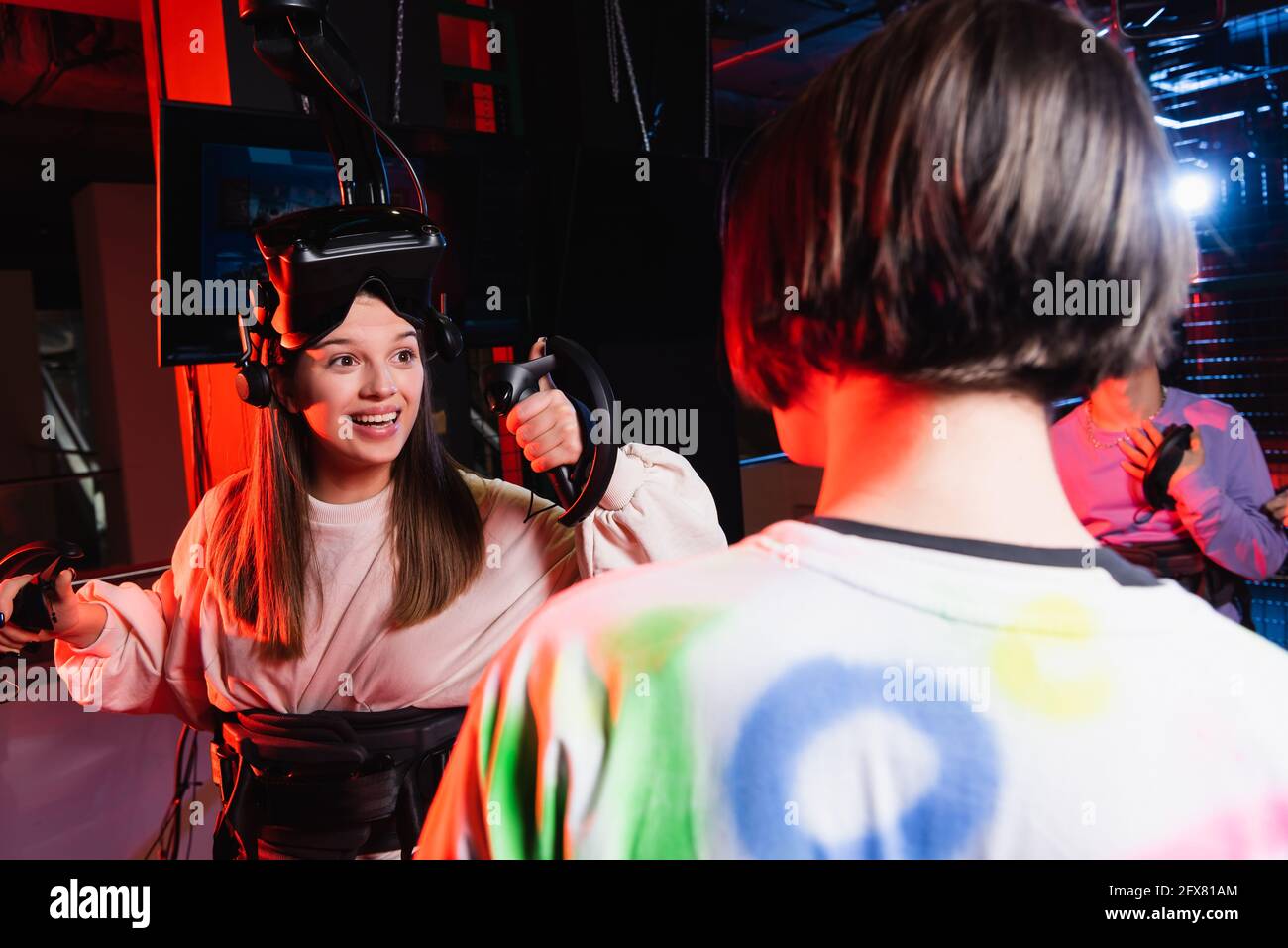 Fröhliches Mädchen lächelt in der Nähe von Teenagerjungen in der VR-Spielzone, verschwommener Vordergrund Stockfoto