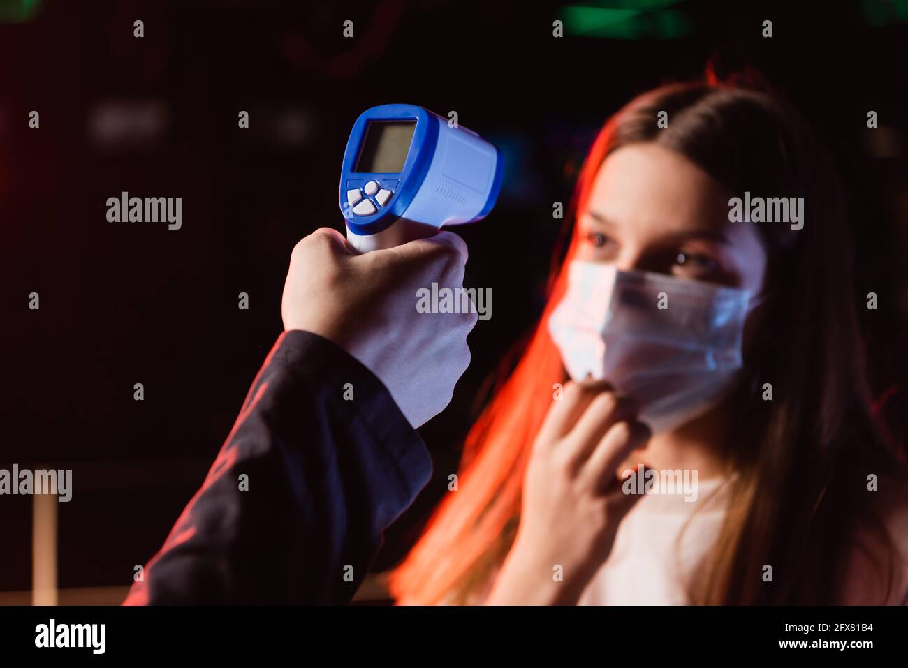 Selektiver Fokus des Pyrometers in der Hand des Controllers nahezu unscharf Teenager-Mädchen in Sicherheitsmaske Stockfoto