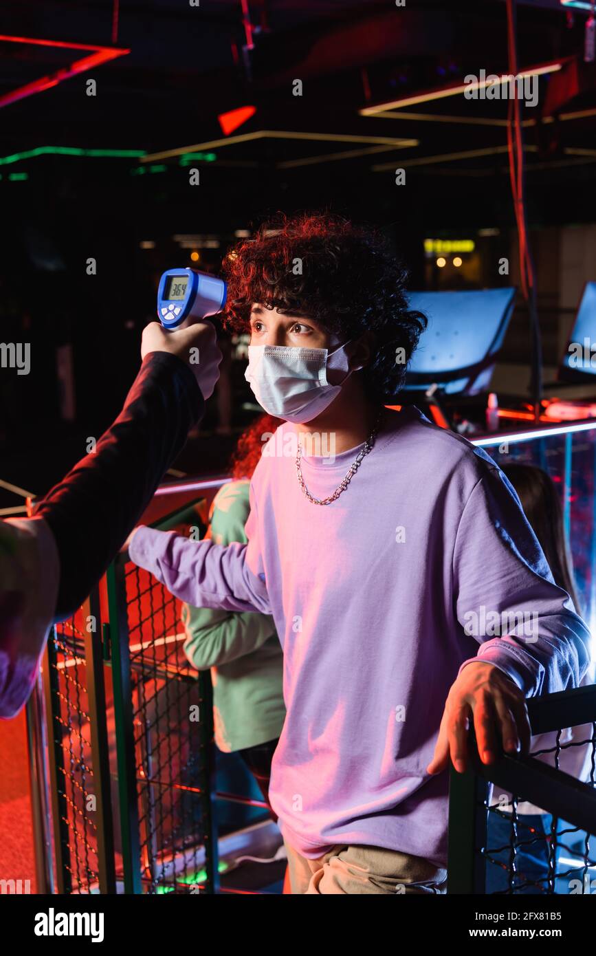 Teenager Junge in medizinischer Maske in der Nähe Controller mit Pyrometer Stockfoto