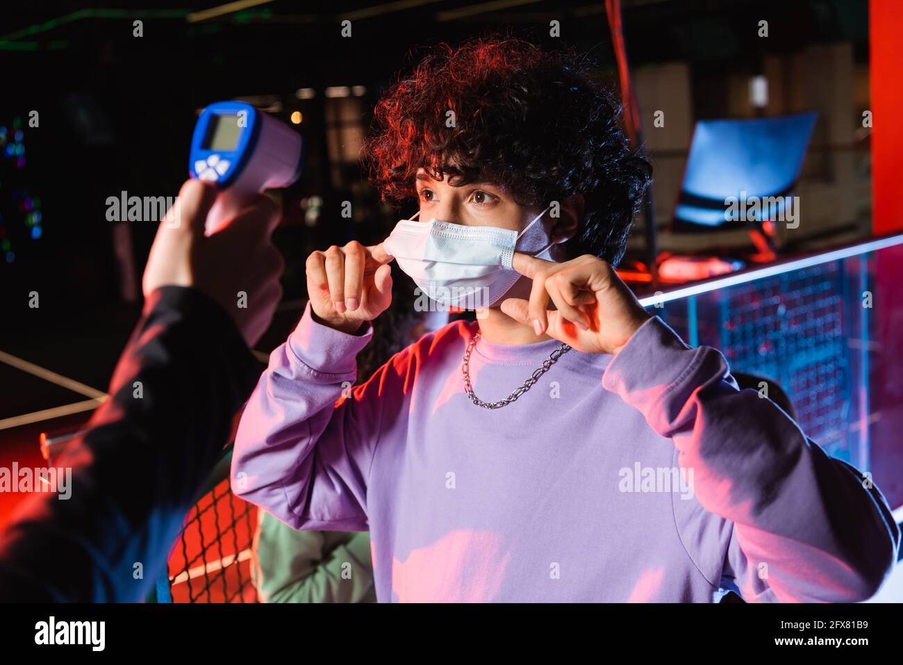Teenager Gamer Anpassung medizinische Maske in der Nähe Controller mit Pyrometer Stockfoto