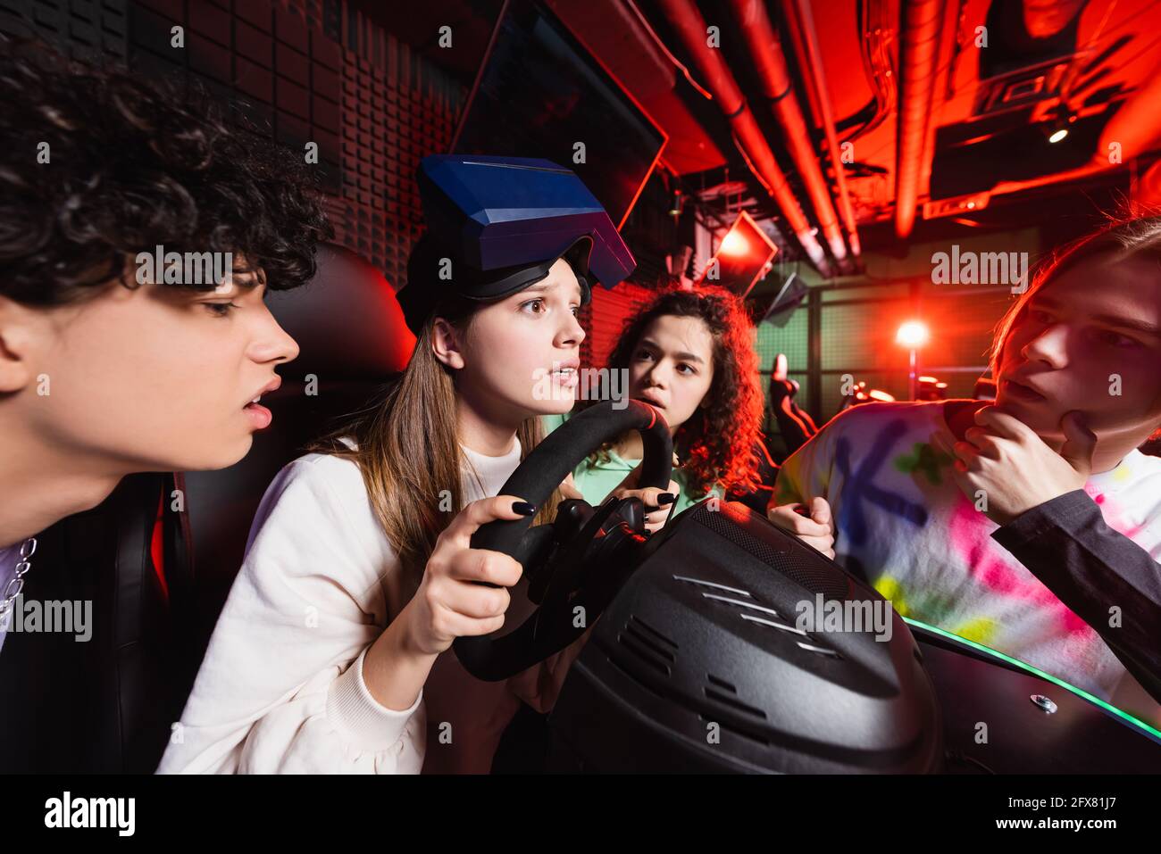 Teenager-Mädchen spielen auf Autorennen Simulator in der Nähe besorgt multiethnisch Freunde Stockfoto