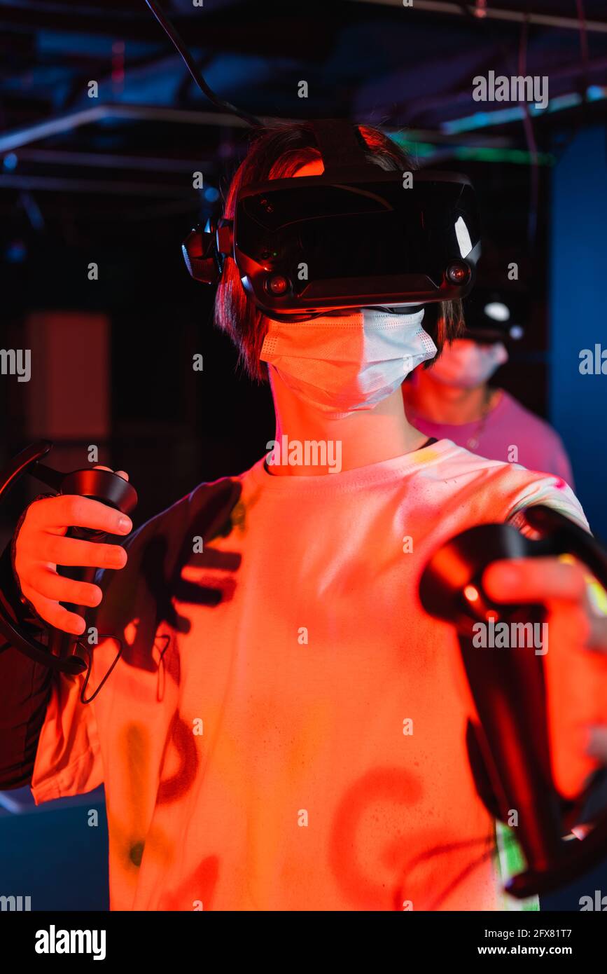 Teenager-Gamer in medizinischer Maske und vr-Headset in der Nähe eines Freundes Auf unscharfem Hintergrund Stockfoto