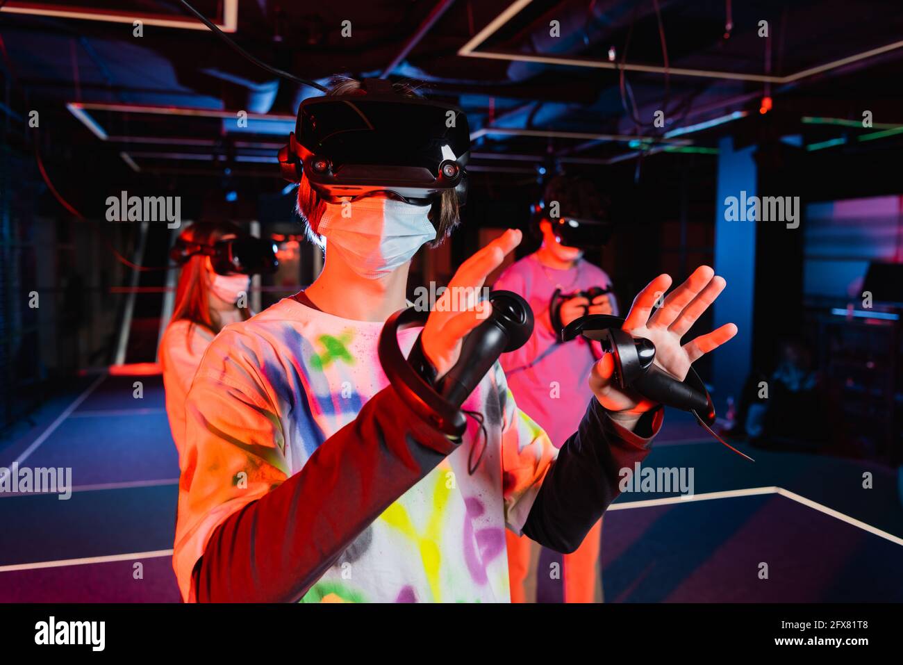 Teenager in medizinischer Maske und vr Headset-Gaming in der Nähe Verschwommene Freunde Stockfoto