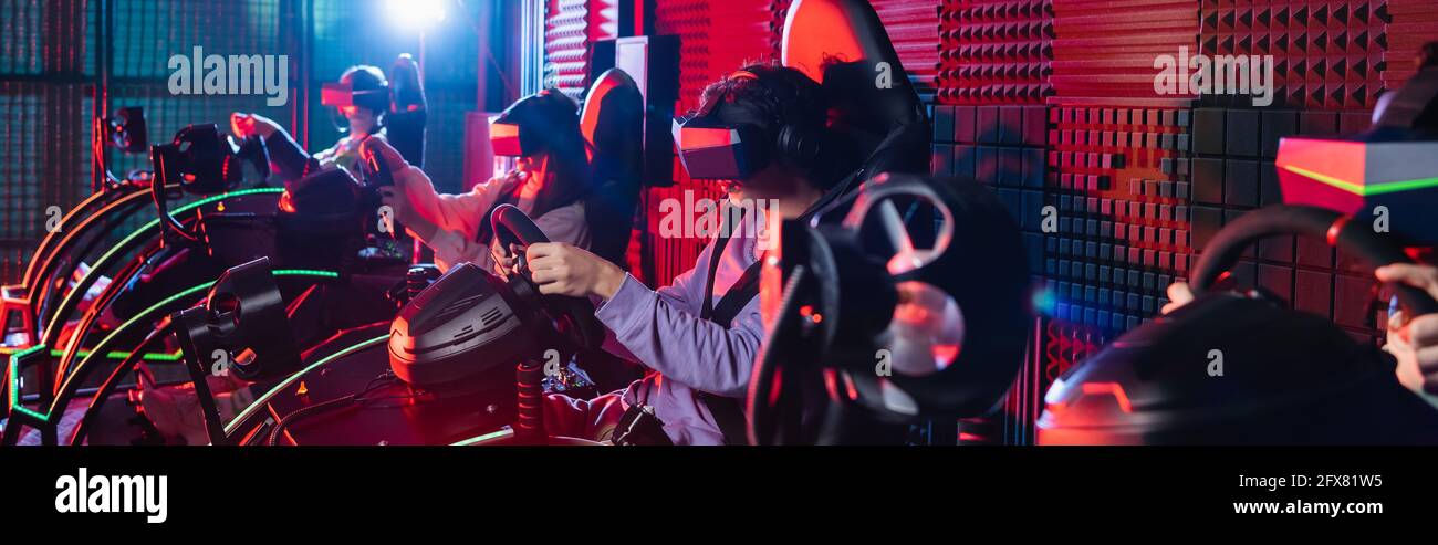 Teenager-Freunde in vr Headsets spielen auf Autorennen Simulatoren, Banner Stockfoto