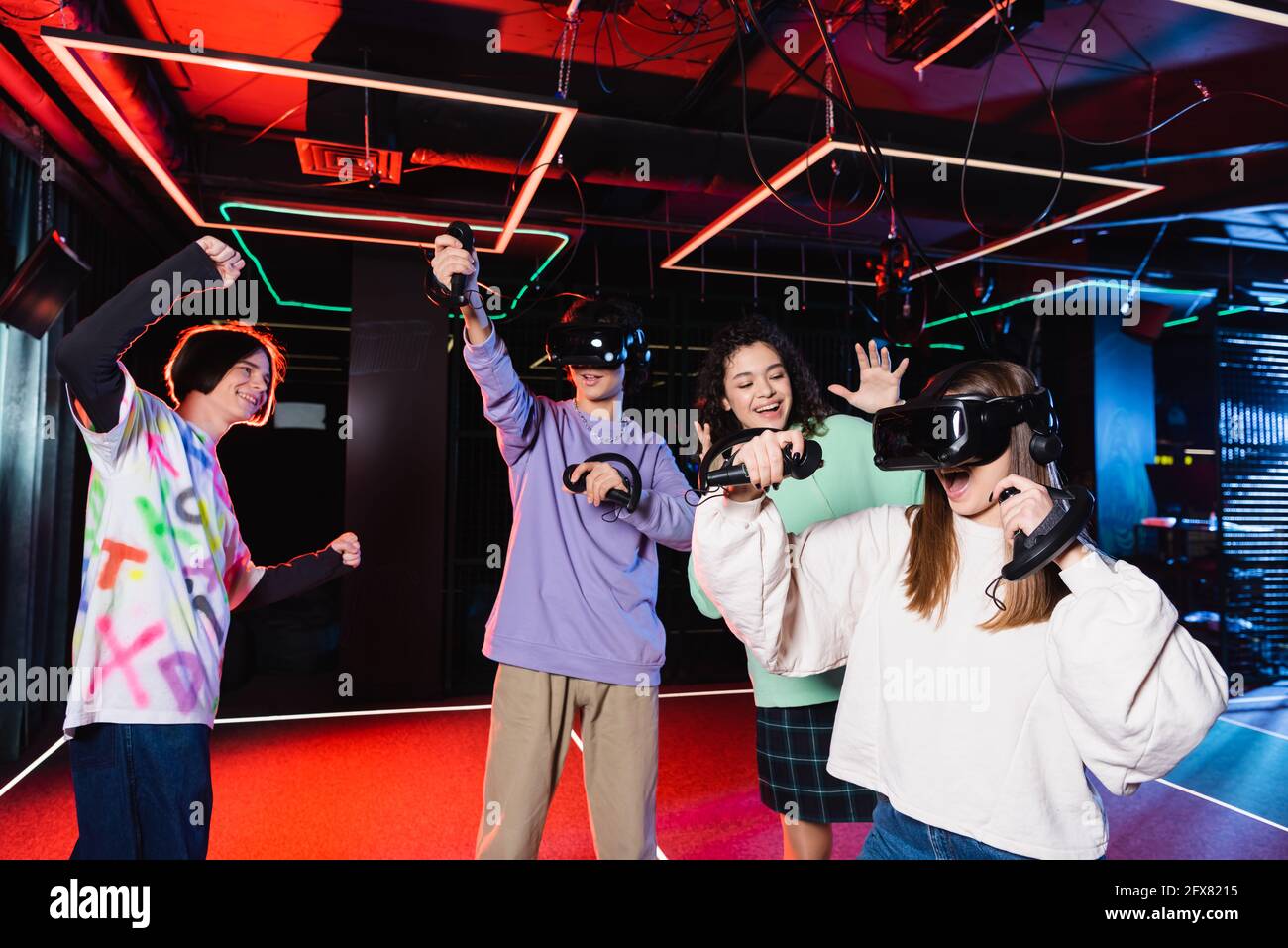Fröhlicher Teenager, der eine Siegesgeste in der Nähe multikultureller Freunde zeigt vr-Spielzimmer Stockfoto