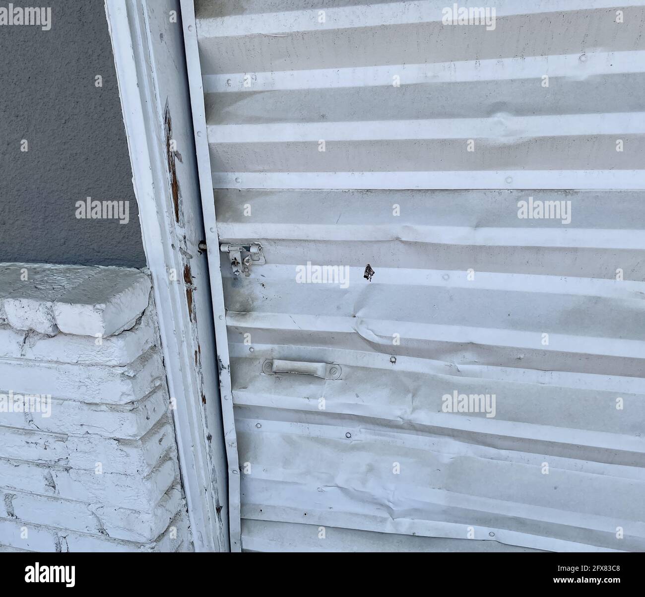 Nahaufnahme eines gebrochenen und verbogenen Metallgaragentor neben einer Ziegelwand Stockfoto