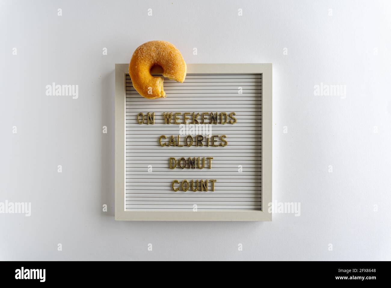 Brieftafel mit Wörtern, die am Wochenende Kalorien Donut Count, in goldenen Buchstaben, mit einem frischen Donut, auf weißem Hintergrund, horizontal Stockfoto