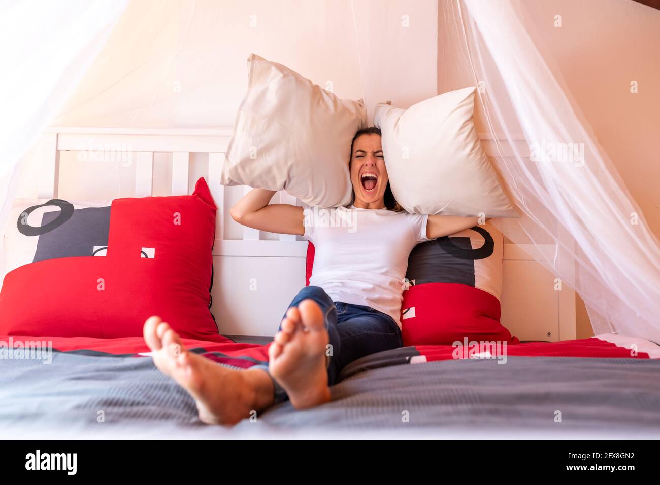 Eine Frau, die im Bett sitzt und Kissen wirft, während sie verrückt und  schreiend wird Stockfotografie - Alamy