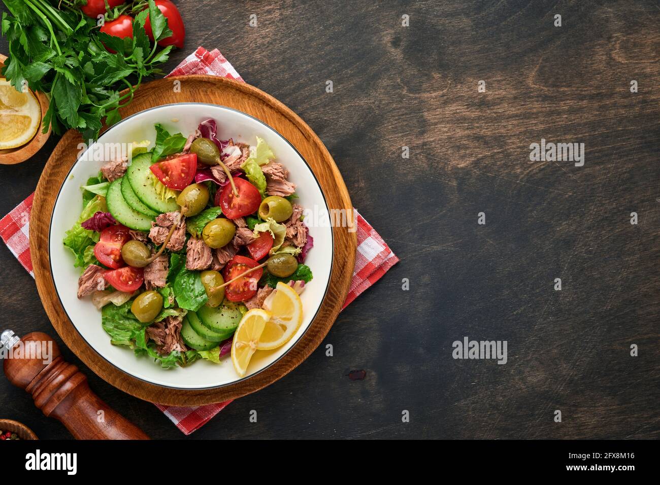 Thunfischsalat mit frischem Gemüse, Oliven, Kapern und Zitrone serviert in einer Schüssel auf altem Holzhintergrund. Draufsicht mit Kopierbereich Stockfoto