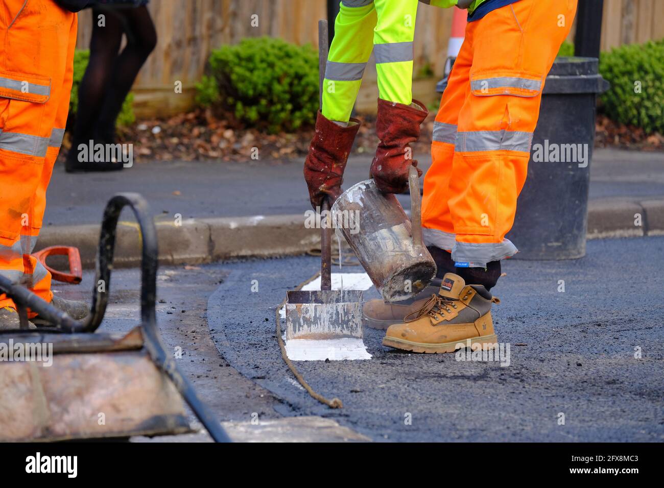 EPSOM, Großbritannien - CIRCA JANUAR 2019:Nahaufnahme, ein Mann in gut sichtbarer Kleidung und harten Stiefeln markiert die Straßenlinien auf einer neu vorbereiteten Straßenoberfläche Stockfoto