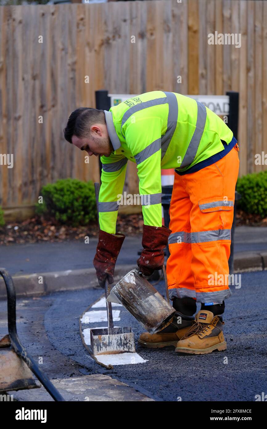 EPSOM, Großbritannien - CA. JANUAR 2019: Ein Mann mit dunklem Haar und gut sichtbarer Kleidung gießt weiße Farbe, um die gepunktete Linie zu markieren Stockfoto