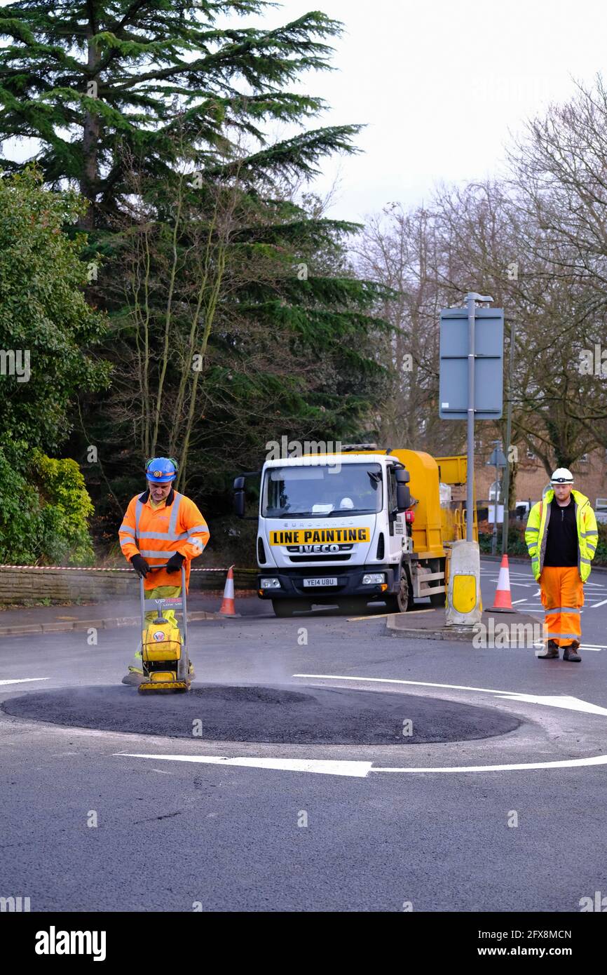 EPSOM, Großbritannien - CA. JANUAR 2019: Mann in gut sichtbarer Kleidung und einem Hut, der die Oberfläche mit einem Verdichter nivellierte Stockfoto