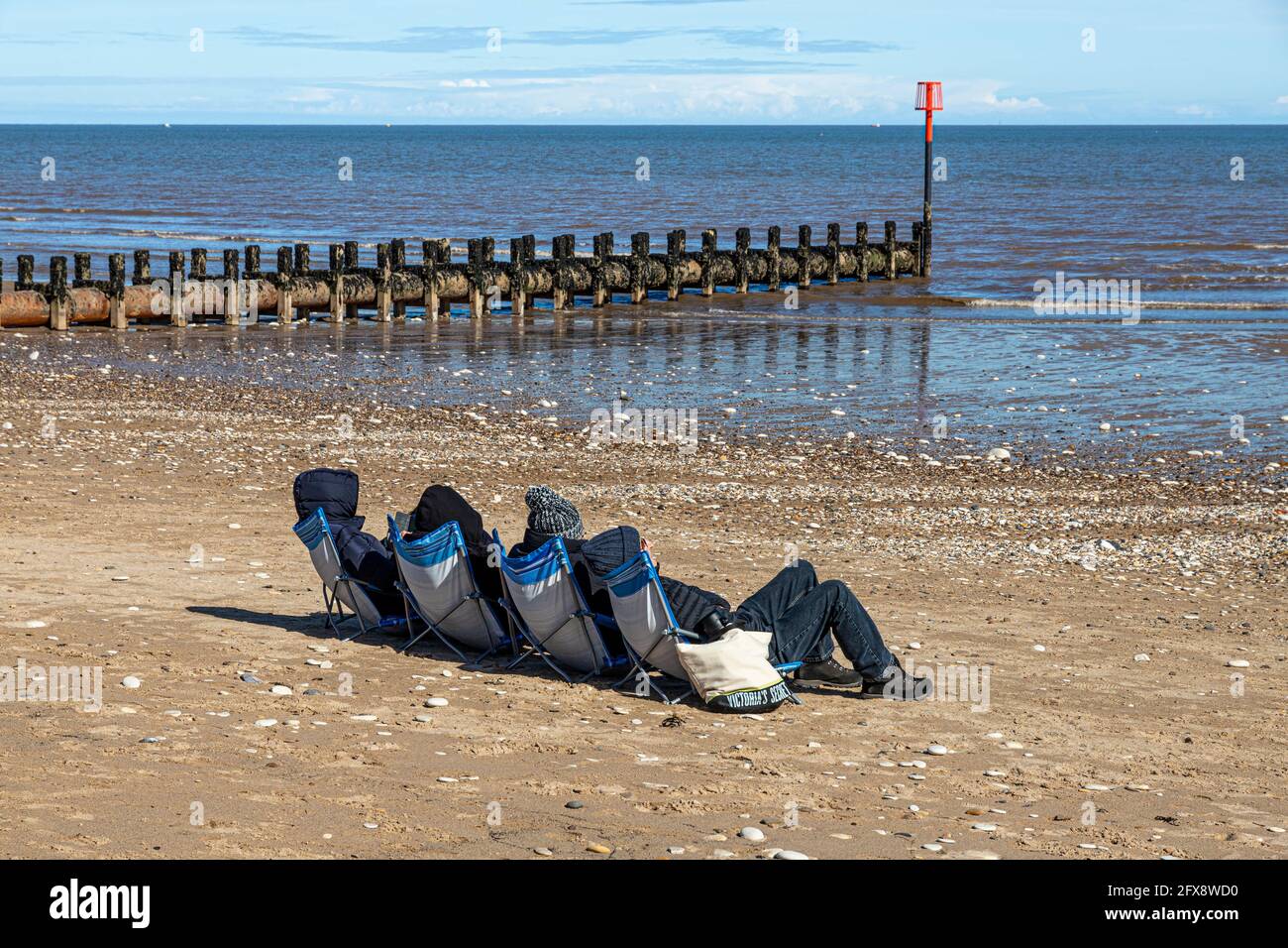 Vier Personen sonnen sich Mitte April an der Nordsee in Bridlington, East Riding of Yorkshire, England. Schwarz-Weiß-Version 2FX8WA1 Stockfoto