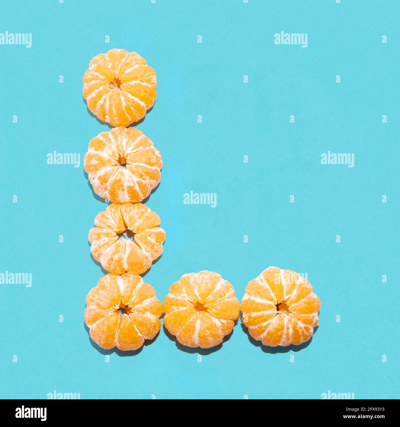 Kreatives Layout des Buchstabens L aus geschälten Mandarinen auf blauem Hintergrund. Flatlay. Stockfoto