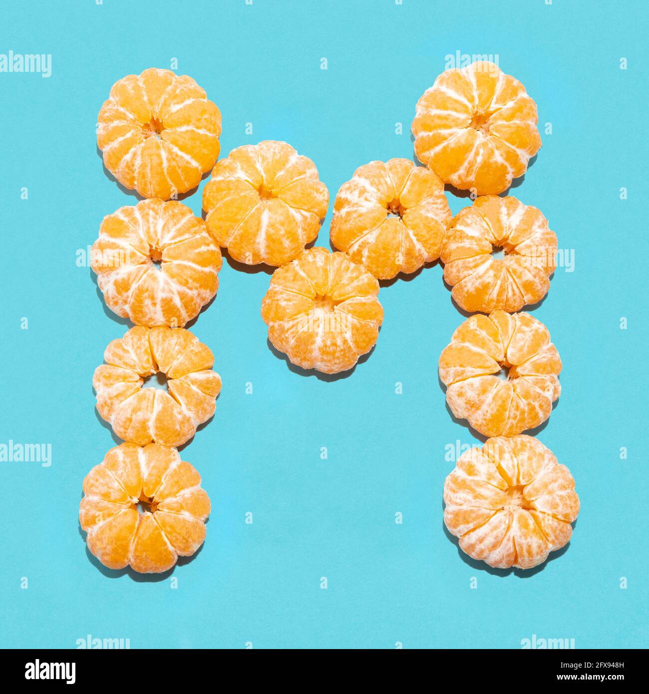 Kreatives Layout des Buchstabens M aus geschälten Mandarinen auf blauem Hintergrund. Flatlay. Stockfoto