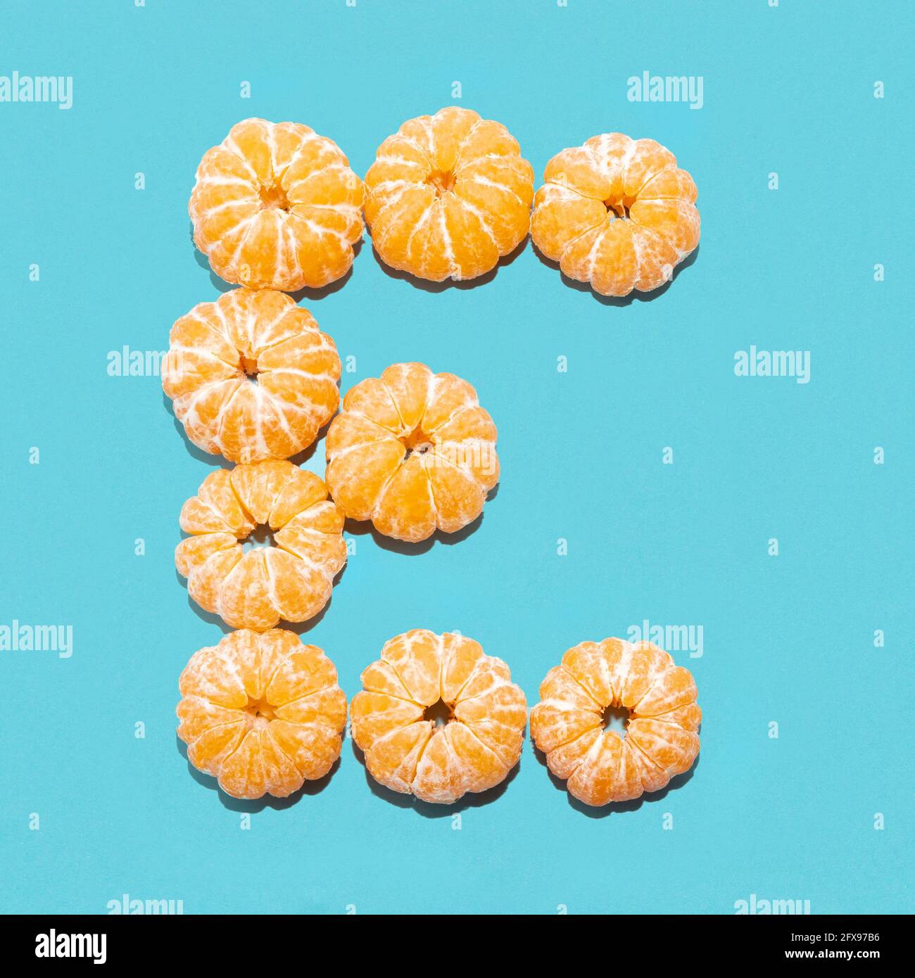 Kreatives Layout des Buchstabens E aus geschälten Mandarinen auf blauem Hintergrund. Flatlay. Stockfoto