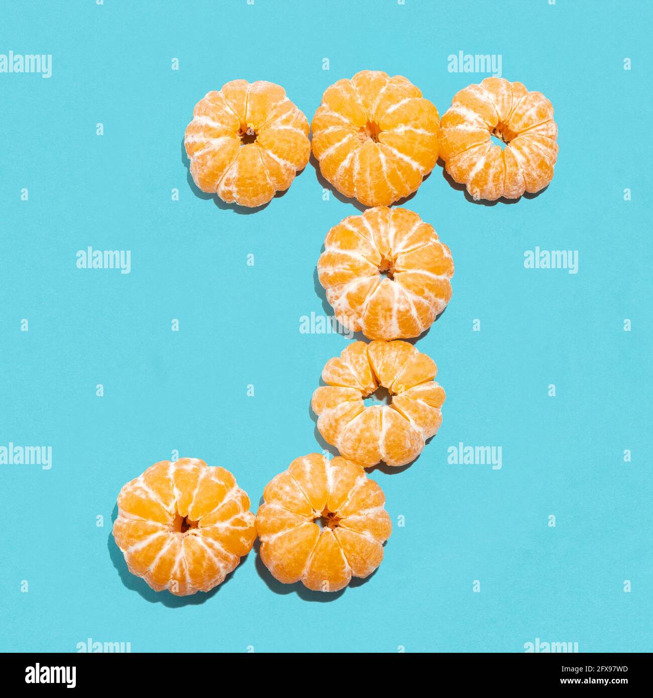 Kreatives Layout des Buchstabens J aus geschälten Mandarinen auf blauem Hintergrund. Flatlay. Stockfoto