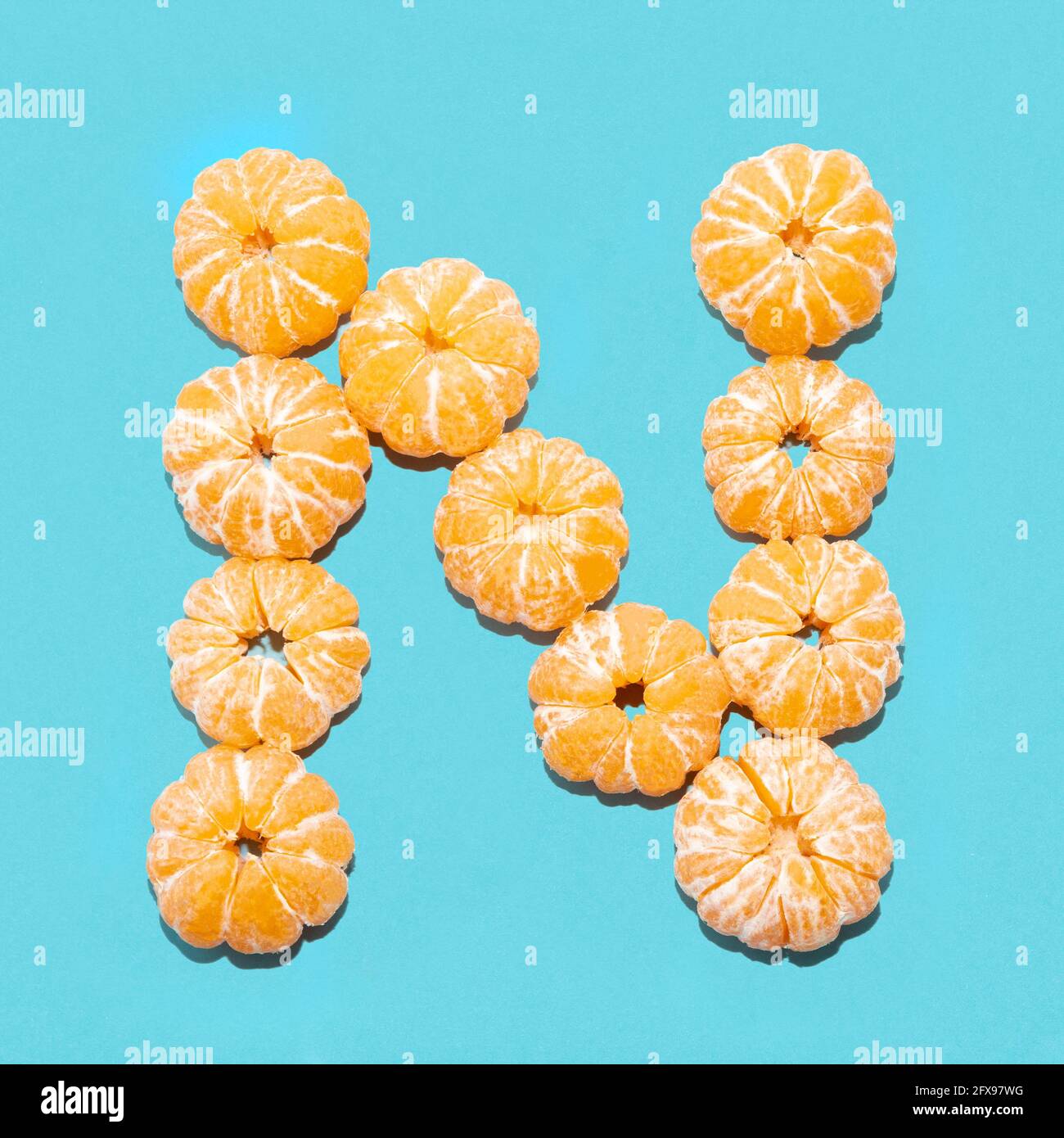 Kreatives Layout des Buchstabens N aus geschälten Mandarinen auf blauem Hintergrund. Flatlay. Stockfoto