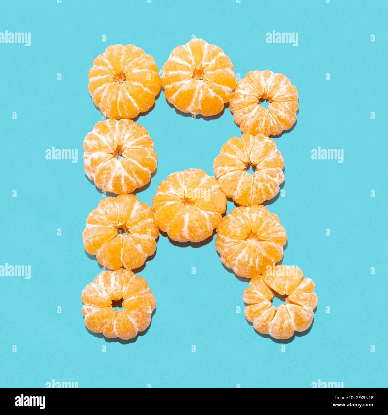 Kreatives Layout des Buchstabens R aus geschälten Mandarinen auf blauem Hintergrund. Flatlay. Stockfoto