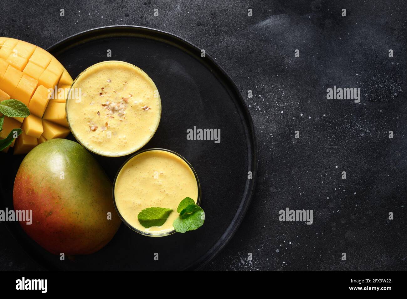 Indische traditionelle kalte Mangolassi oder Smoothies auf schwarzem Hintergrund, Draufsicht mit Kopierraum. Gesunde Lassi aus Joghurt, Wasser, Gewürzen, Früchten und Stockfoto
