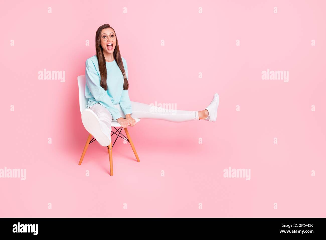 In voller Größe Porträt der fröhlichen Person heben die Beine öffnen Mund Tragen Sie einen hellblauen Pullover auf rosa Hintergrund isoliert Stockfoto