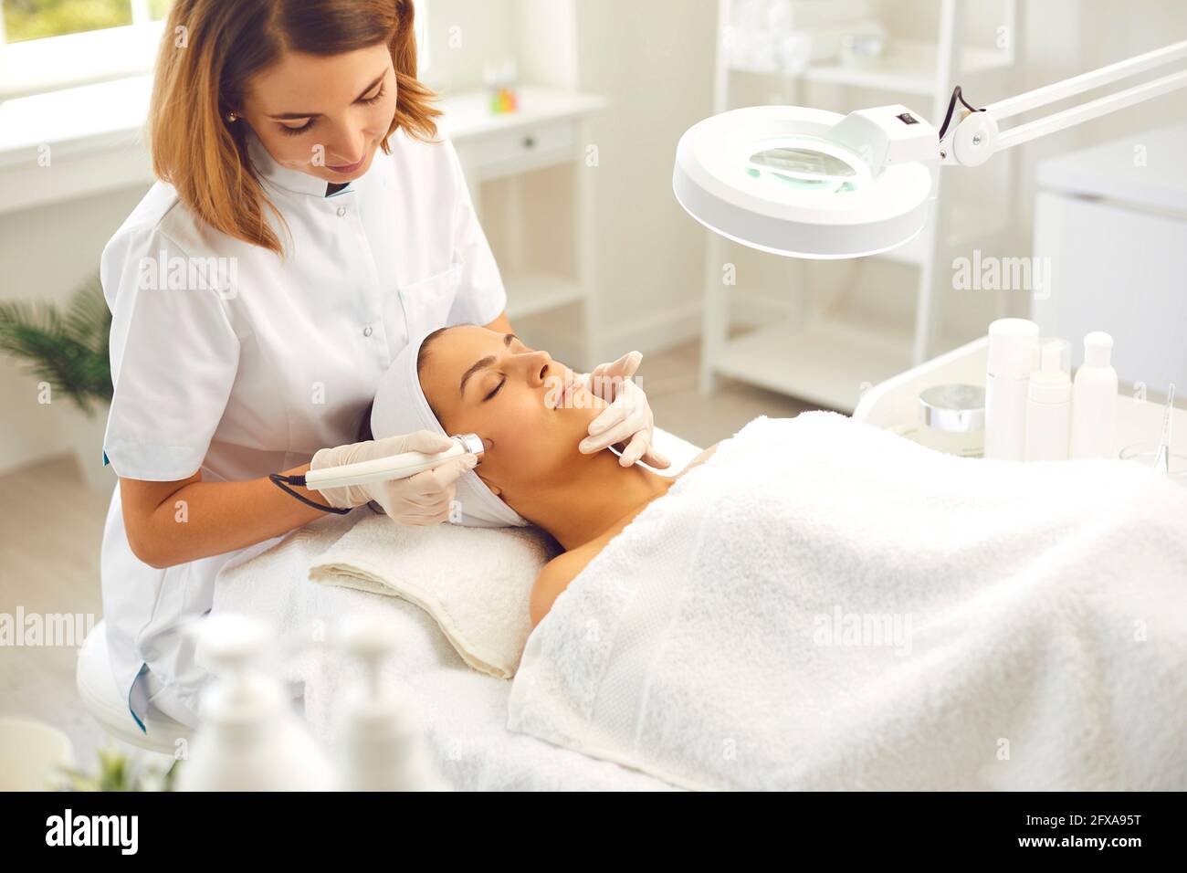 Lächelnder Dermatologe macht Hautpflege Verfahren Ultraschall Mikrodermabrasion für Frau in Schönheitssalon Stockfoto