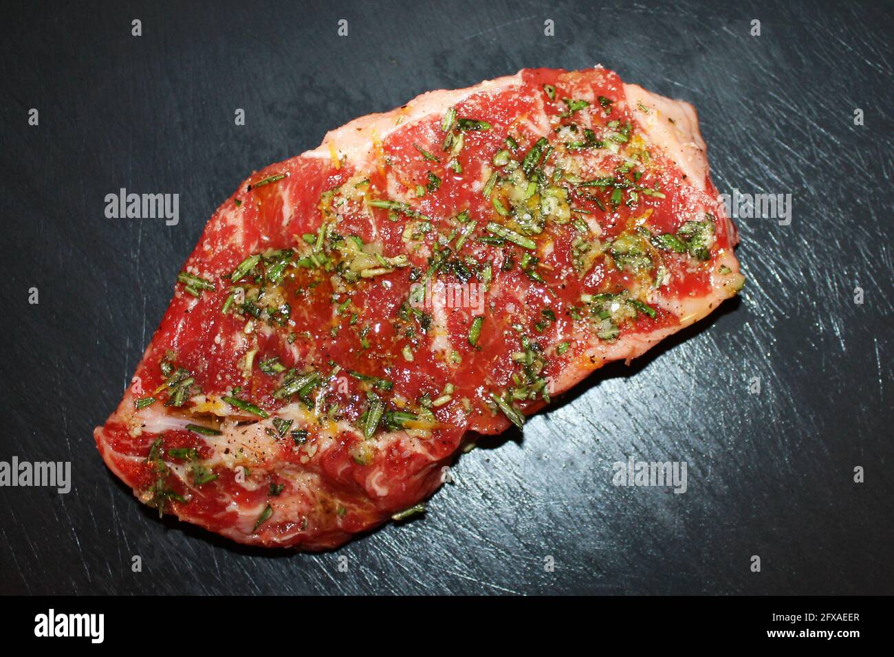 Nahaufnahme von ungekochten Rindfleisch, gewürzt mit Salz, Pfeffer, Basilikum und Zitronenschale, auf einem Schneidebrett aus schwarzem Stein. Stockfoto