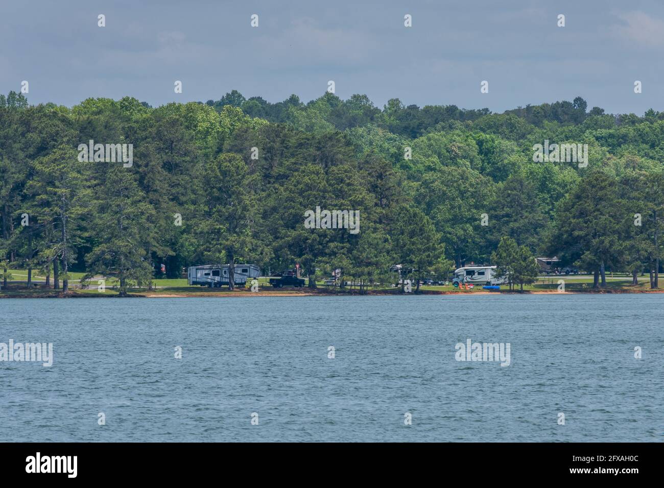 Über den See ist ein Campingplatz am Wasser mit Camper und Zelte Picknicktische und Klappstühle aufgestellt Für einen Kurzurlaub auf einer heißen, feuchten da Stockfoto