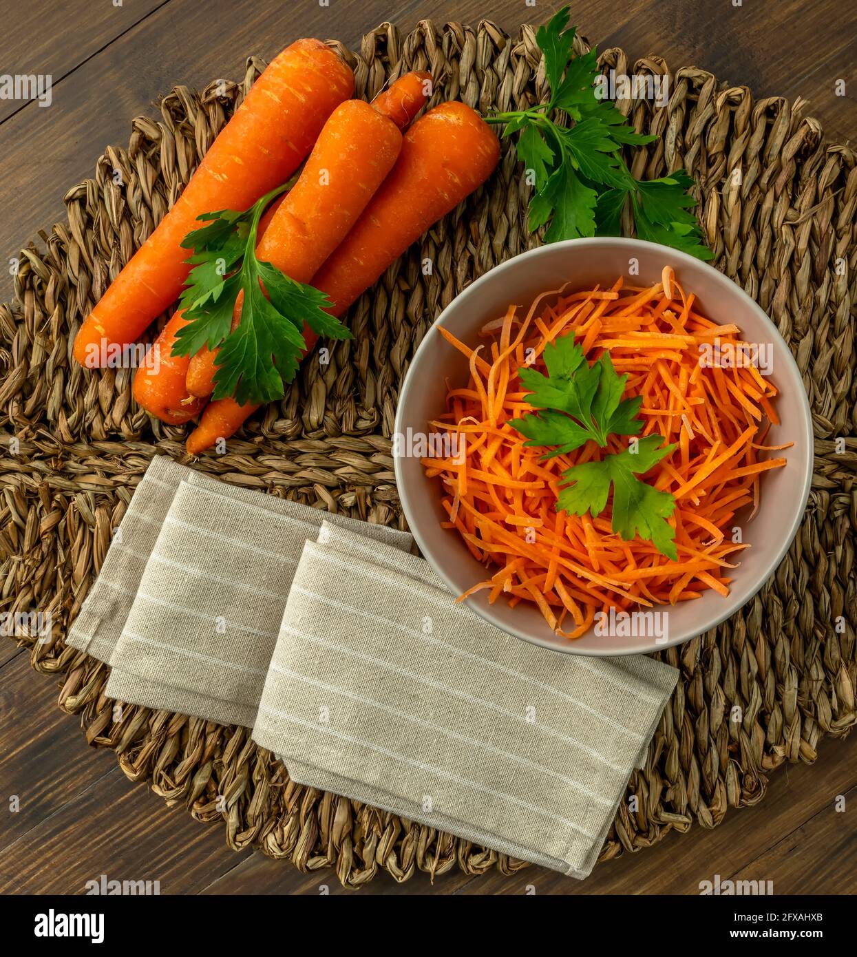 Zusammensetzung von ganzen und entsafteten Karotten auf einer Strohmatte Mit Petersilienblättern und beiger Serviette Stockfoto