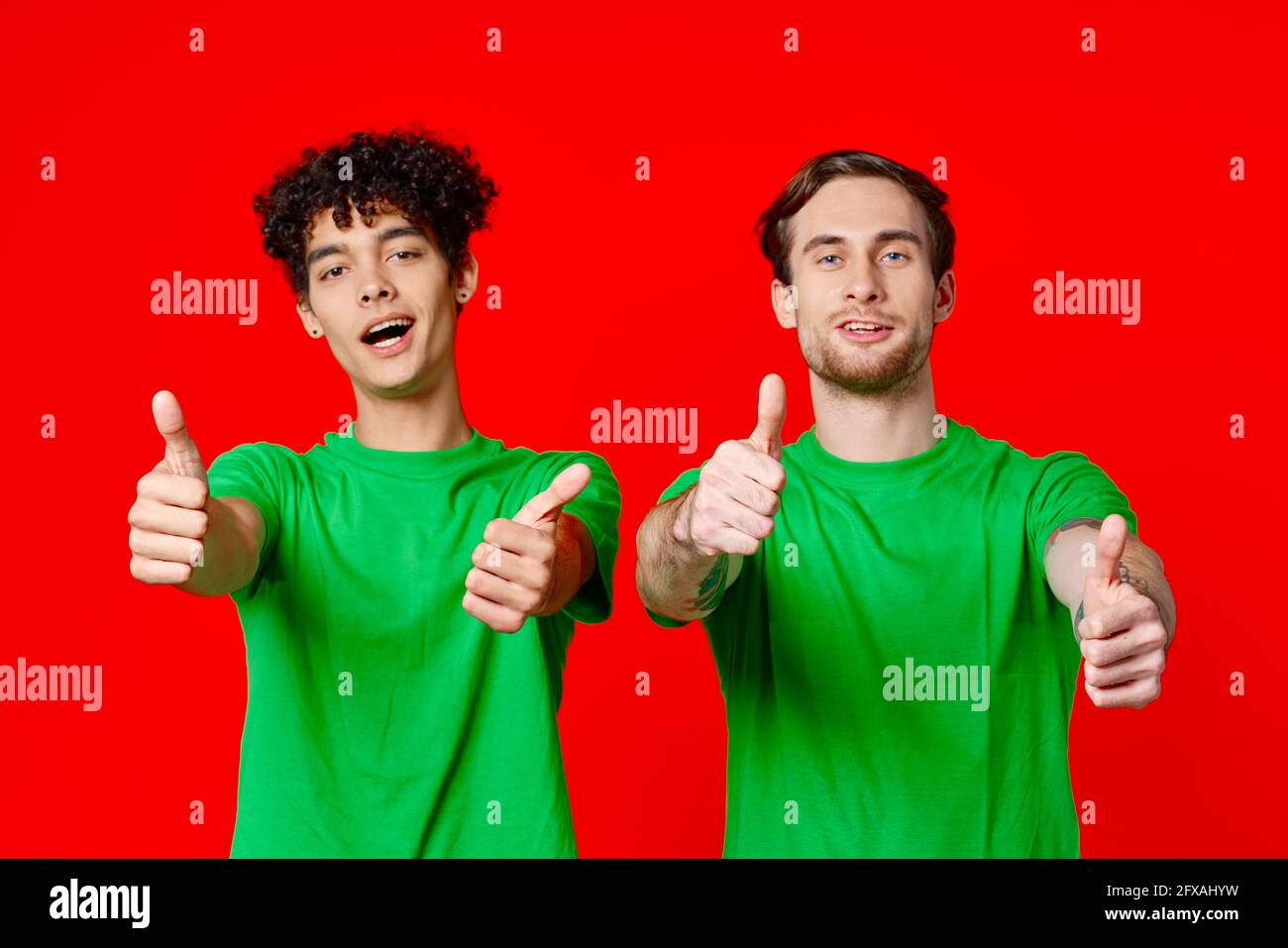 Fröhliche Freunde in grünen T-Shirts gestikulieren mit Händen Emotionen rot Hintergrund Stockfoto