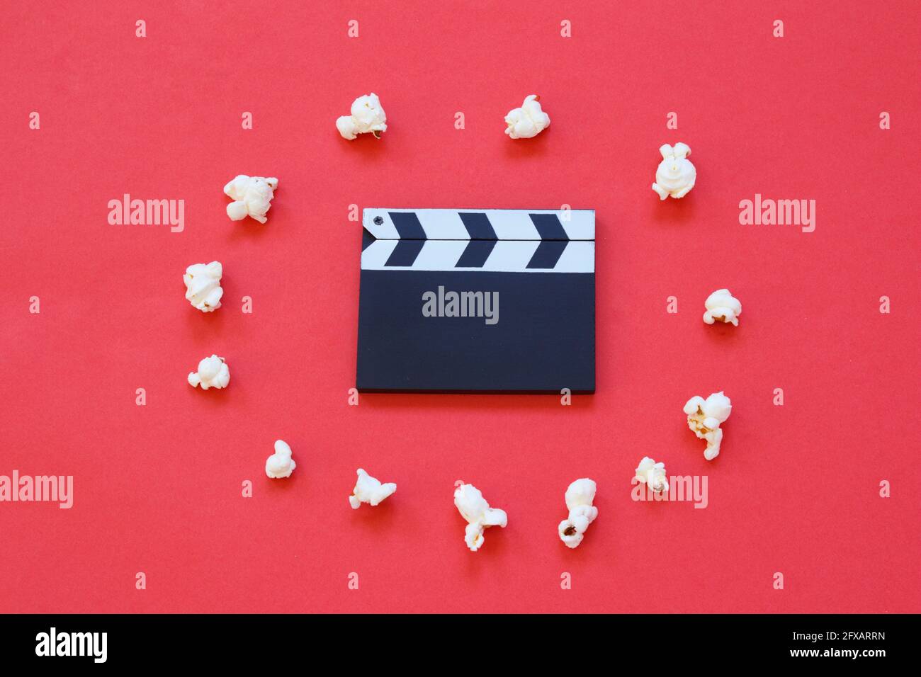 Filmklapperboard und Popcorn isoliert auf rotem Hintergrund. Unterhaltungsbranche. Filmzeit. Minimalistischer Hintergrund. Stockfoto