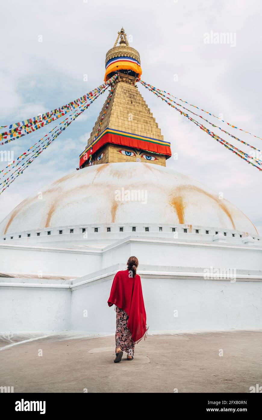 Weiblich gekleidetes langes Sommerkleid mit rotem Schal, das am Platz in der Nähe von Boudhanath Stupa vorbei geht - den größten kugelförmigen Stupas in Nepal. Reisen durch den Stockfoto