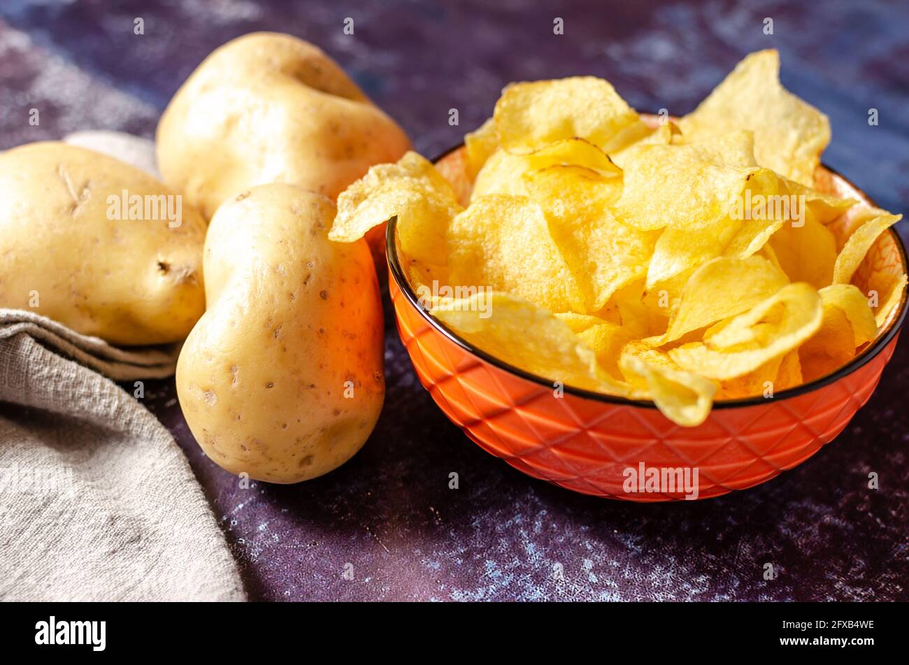 Stillleben einer Schüssel Kartoffelchips mit rohen Kartoffeln und einem Leinentuch. Stockfoto