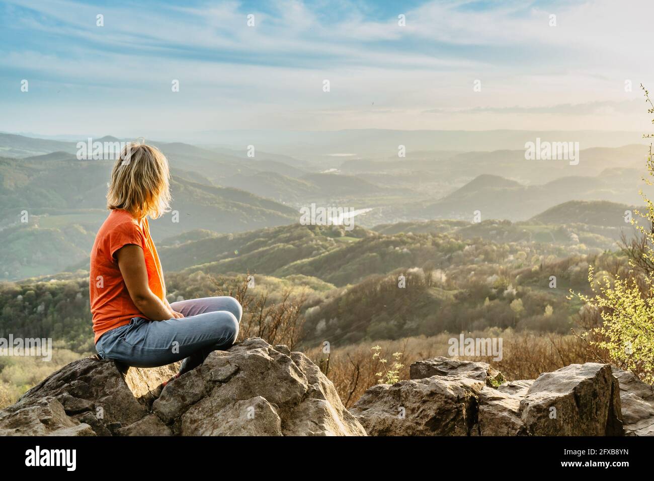 Weibliche Reisende mit friedlichem Geist sitzen auf Felsen und genießen die Aussicht Von Frühling üppiges Tal bei Sonnenuntergang.Wandertag aktiven Lebensstil.Wanderlust Frau Stockfoto