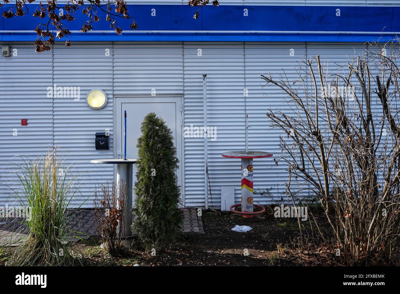 Zwei Bistro-Bartische vor einer Snackbar, die sich in einem Behälter mit eingeschalteter Lampe an der Wand befindet. Stockfoto