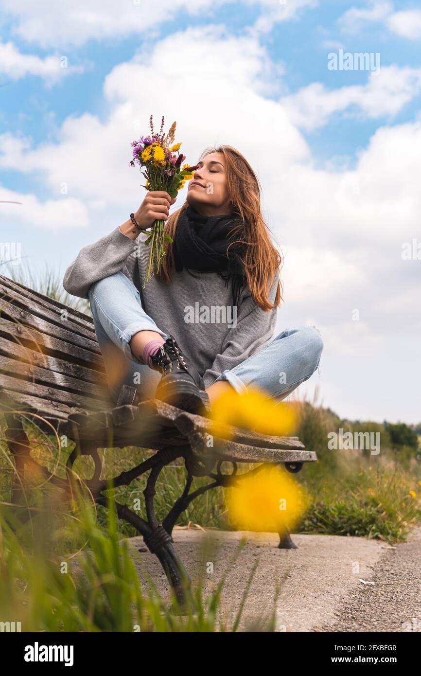 Junge Frau riecht Blumen auf der Bank in der Natur Stockfoto