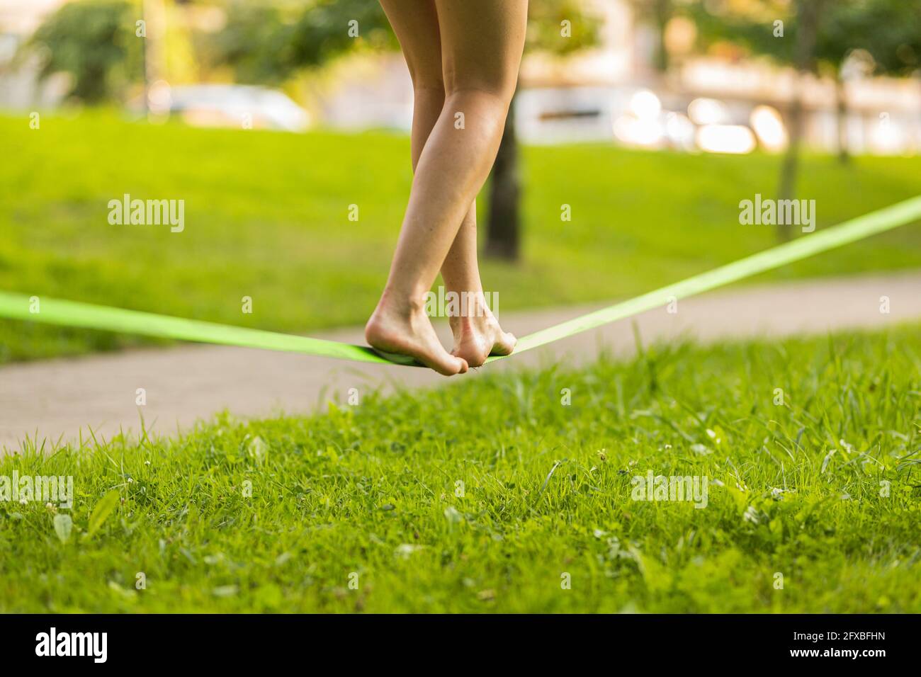 Junge Frau balanciert barfuß auf Slackline im öffentlichen Park Stockfoto