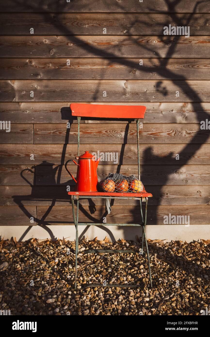 Becher aus rotem Emaille mit Äpfeln auf dem Stuhl im Hinterhof Stockfoto