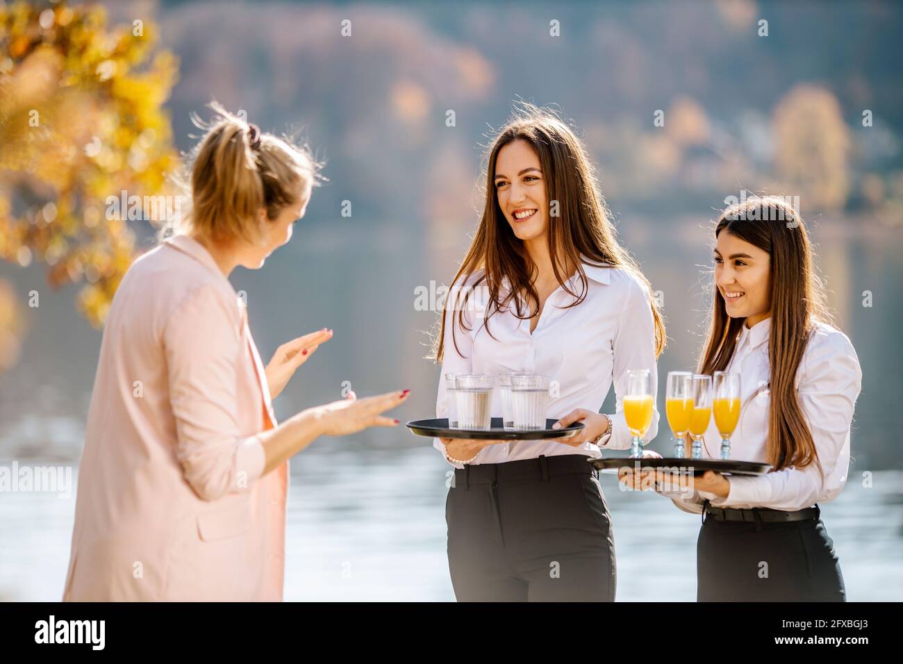 Weibliche Veranstaltungsplanerin weist Kellnerin an, die Getränkeschalen hält Stockfoto