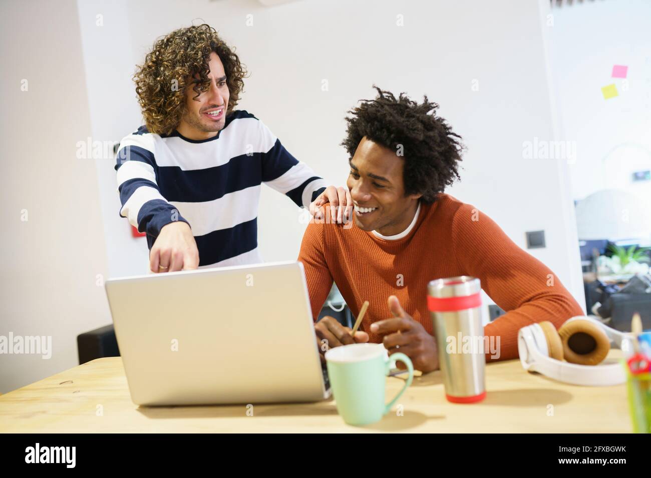 Lächelnde, multiethnische, kreative Geschäftsleute diskutieren im Büro über einen Laptop Stockfoto